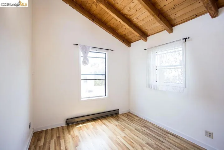 Room featuring two windows, wood-finish flooring, and a vaulted ceiling with exposed wood beams