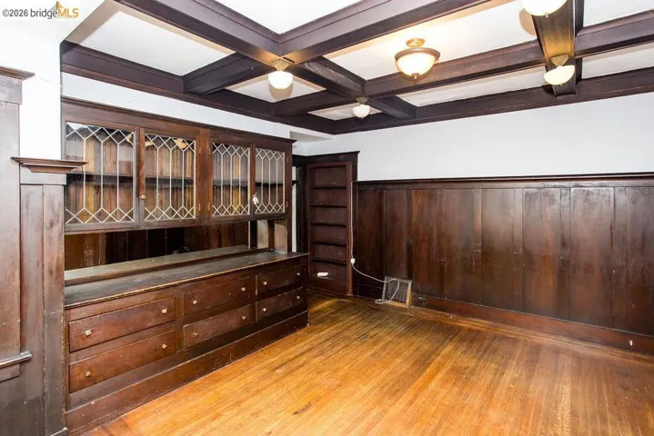 Room featuring wood-finish flooring, dark wood wainscoting, and an exposed beam ceiling