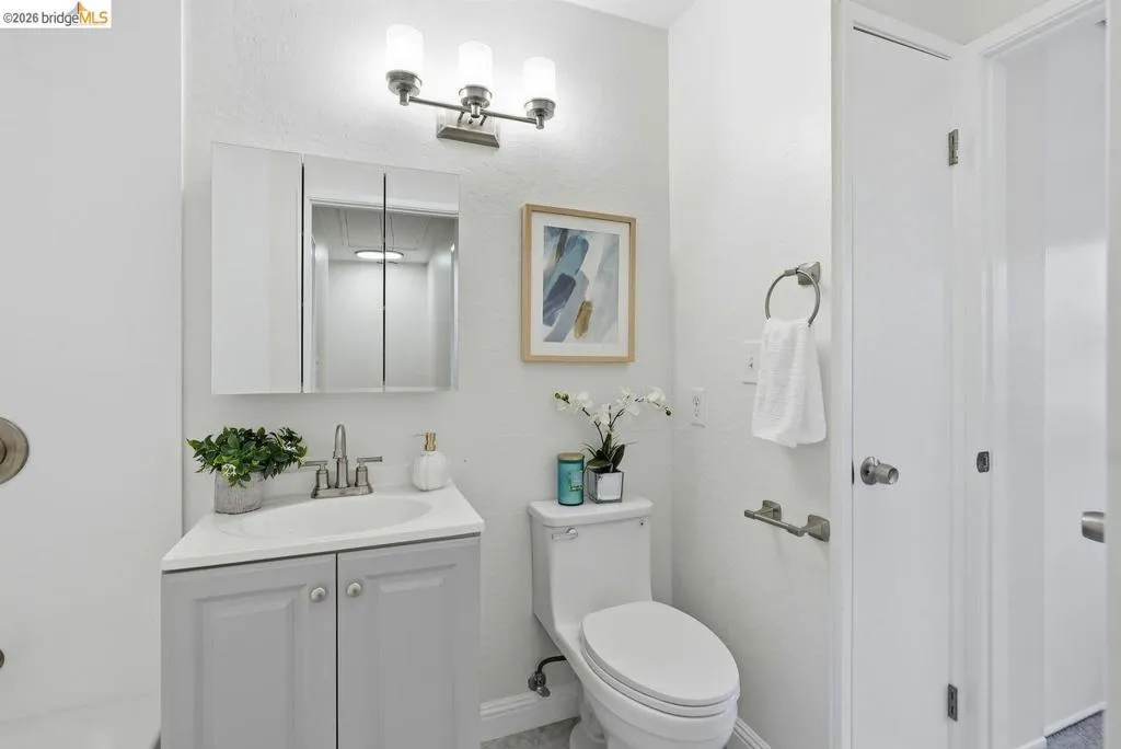 Bathroom featuring a light gray vanity with an integrated sink, tri-fold mirrored medicine cabinet, brushed nickel light fixture, and white toilet