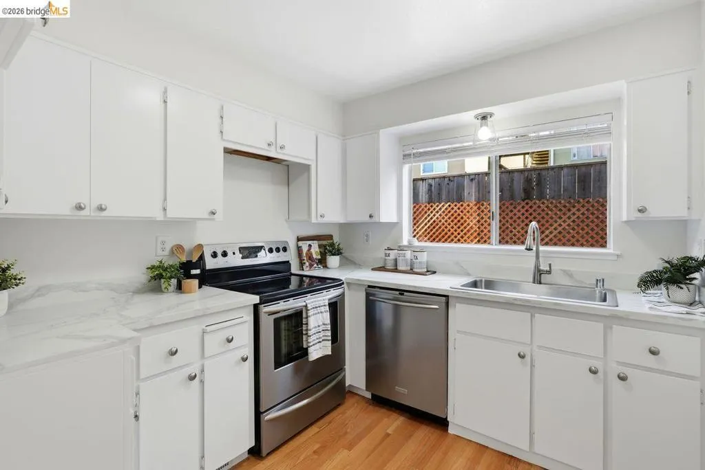 Updated kitchen featuring white cabinetry, stone-finish countertops, stainless steel appliances, and wood-finish flooring