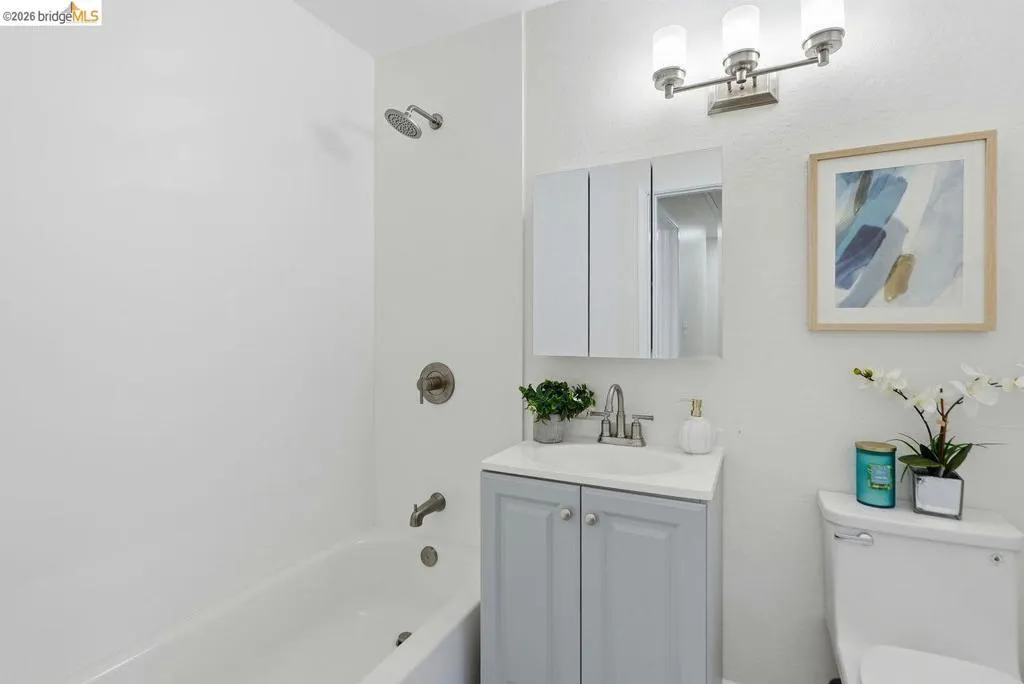 Bathroom featuring a white bathtub, brushed nickel fixtures, a light gray vanity with an integrated sink, a mirrored medicine cabinet, and a three-light vanity fixture