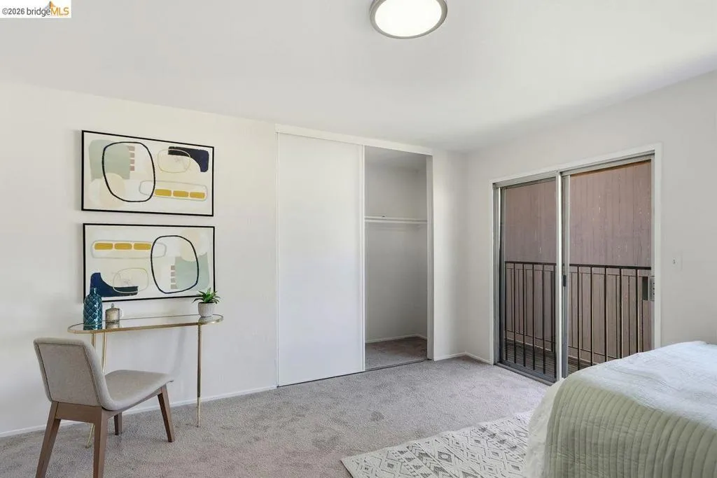 Juliet balcony light-filled room featuring neutral wall paint, gray carpeting, a built-in closet with sliding doors, a flush-mount ceiling light fixture, and glass sliding doors with a black metal railing