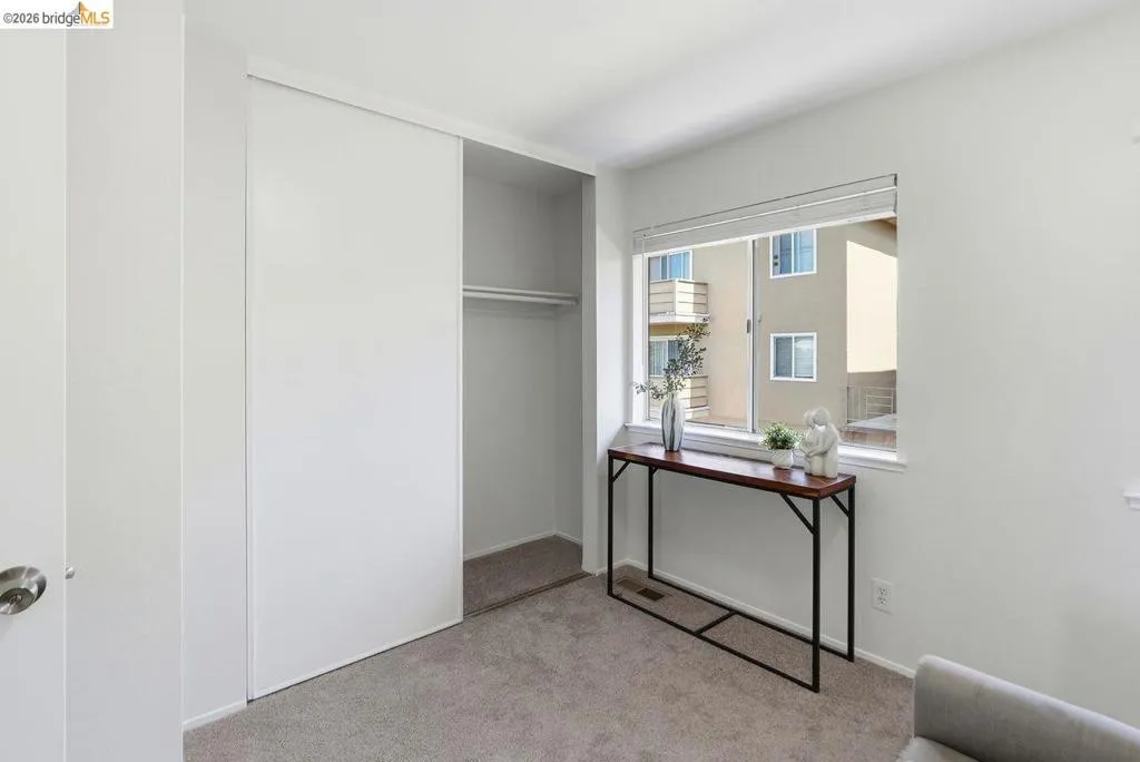 Neutral wall paint throughout, featuring a window with horizontal blinds, carpet flooring, and a closet with sliding doors