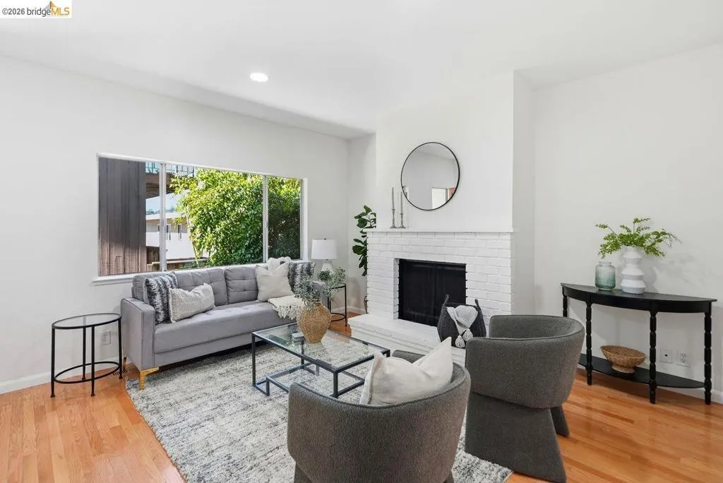 Living area featuring a white brick fireplace, wood-finish flooring, recessed lighting, and a large picture window