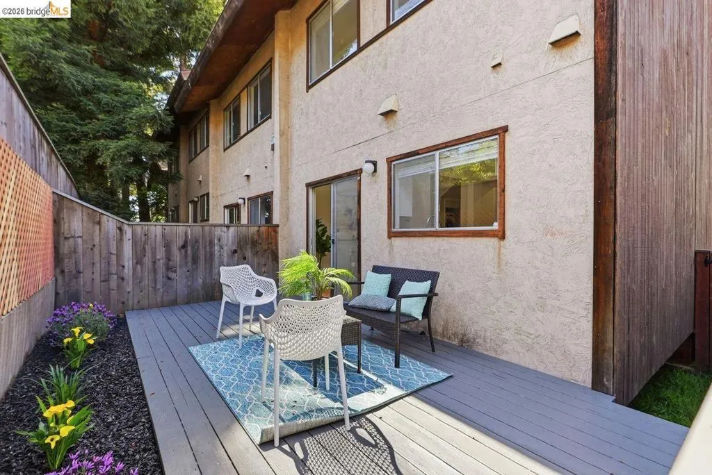 Private outdoor patio featuring a gray deck, a wood privacy fence, and a landscaped planting area with flowers
