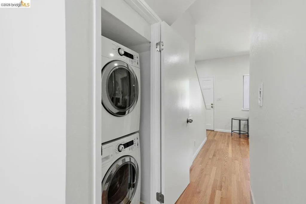 Dedicated laundry closet featuring a stackable washer and dryer, wood-finish flooring, white painted walls, and a staircase with white risers