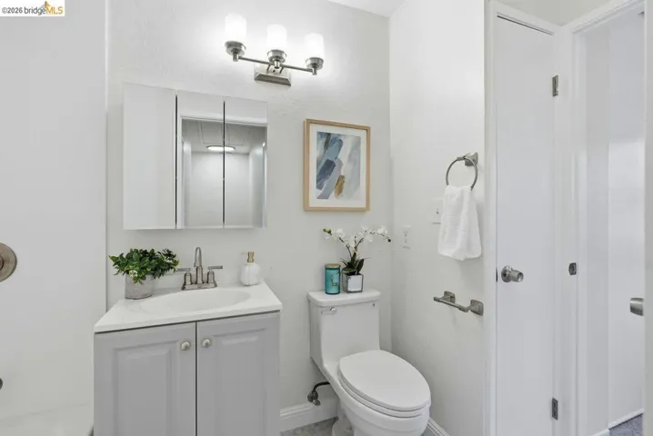 Bathroom featuring a light gray vanity with an integrated sink, tri-fold mirrored medicine cabinet, brushed nickel light fixture, and white toilet