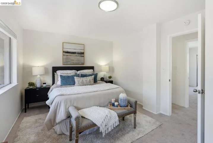 Bright bedroom featuring a large window, plush carpeting, and a flush-mount ceiling light