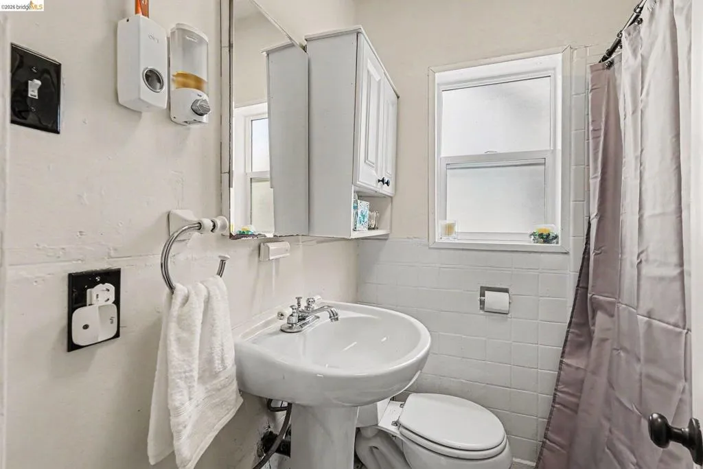 Pedestal sink with chrome fixtures, medicine cabinet with mirrored door, and a shower area with a curtain rod