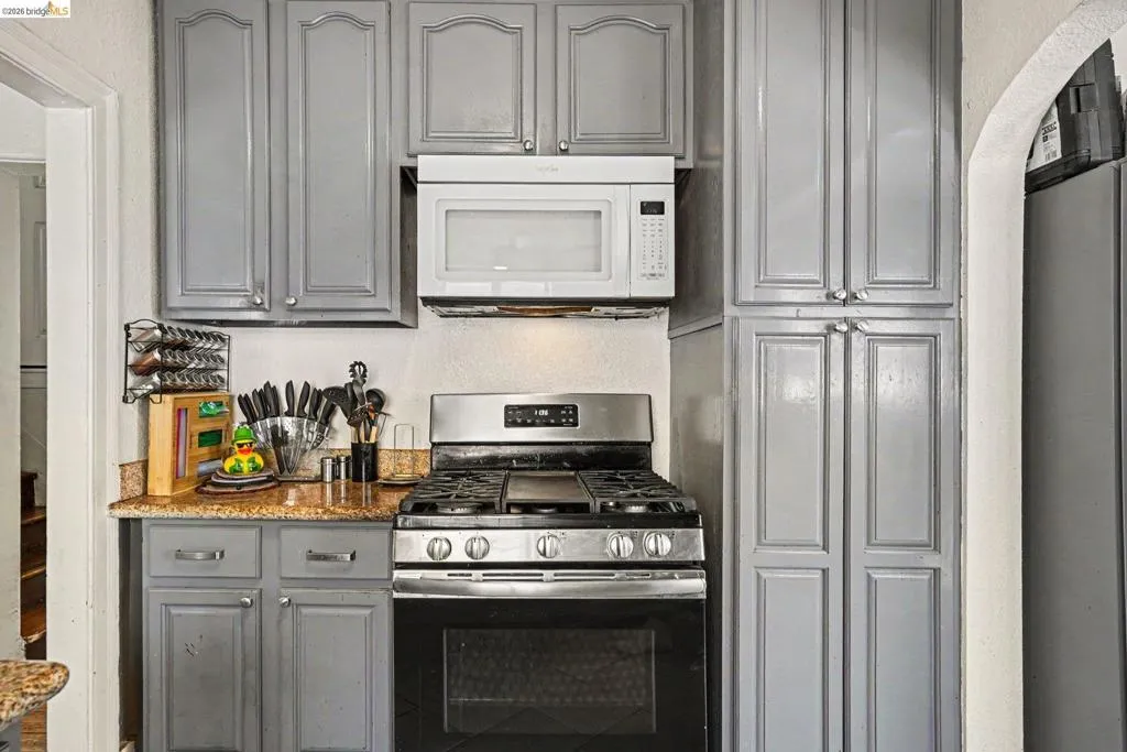 Kitchen featuring gray cabinetry, stainless steel gas range, over-the-range microwave, and a flecked countertop