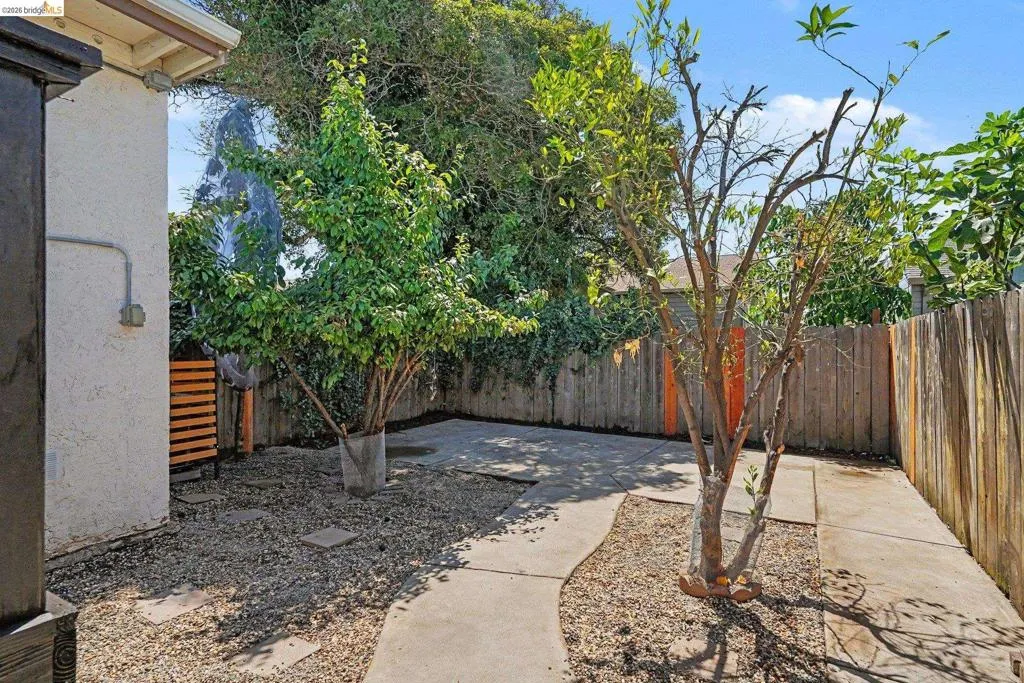 Private outdoor space featuring concrete pathways, gravel landscaping, and mature trees