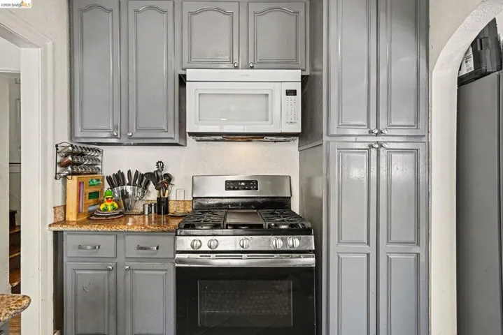 Kitchen featuring gray cabinetry, stainless steel gas range, over-the-range microwave, and a flecked countertop