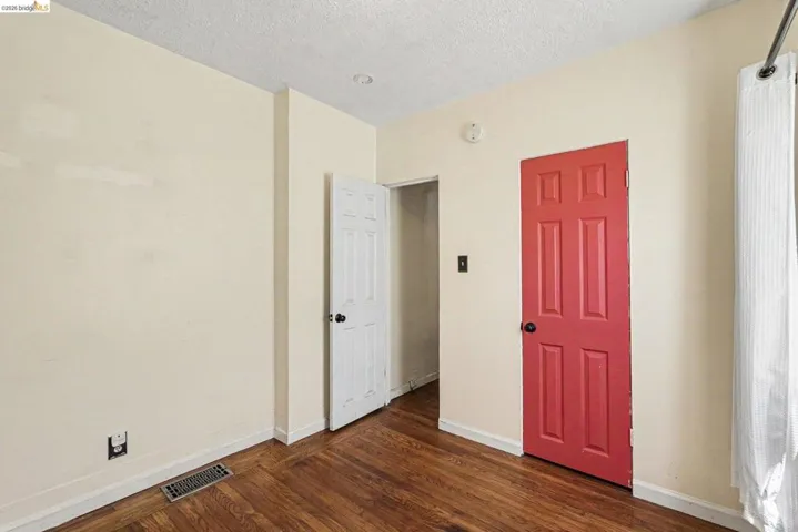 Room featuring warm cream-painted walls, wood-finish flooring, white trim, a red paneled door with black hardware, and a white paneled door with black hardware
