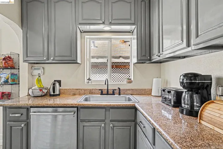 Kitchen featuring gray cabinetry, a stainless steel sink with a matte black faucet, and speckled countertops