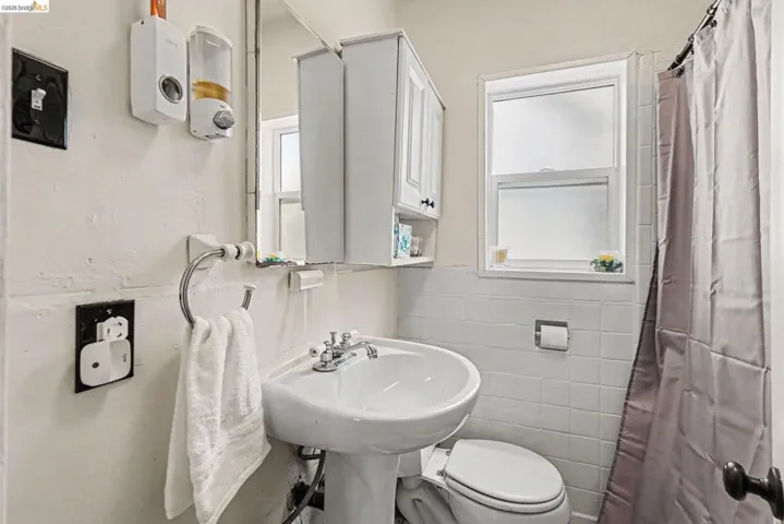 Pedestal sink with chrome fixtures, medicine cabinet with mirrored door, and a shower area with a curtain rod