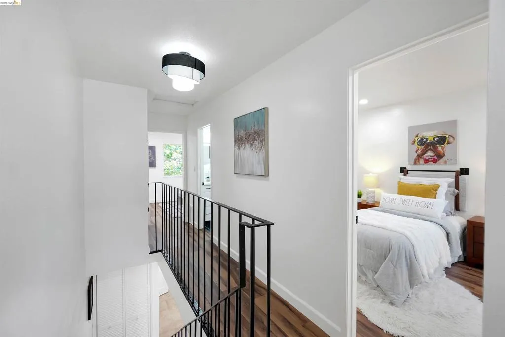 Upper-level hallway featuring wood-finish flooring, a contemporary ceiling fixture, and a black metal railing overlooking the lower level