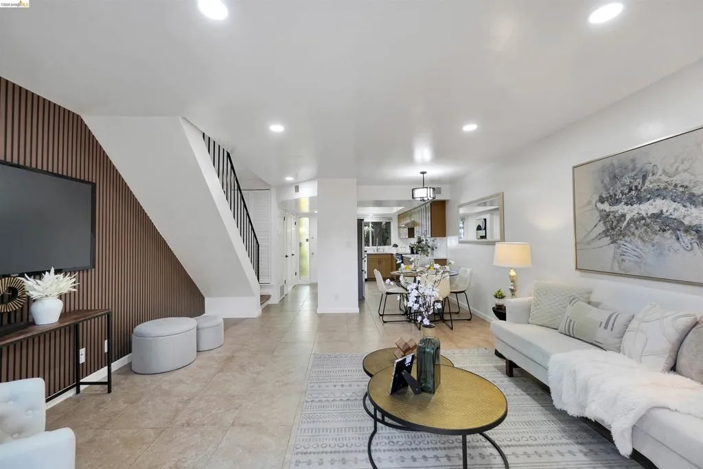 Open-concept living area featuring tile flooring, recessed lighting, a contemporary wood-slat accent wall, and a staircase with black metal railings