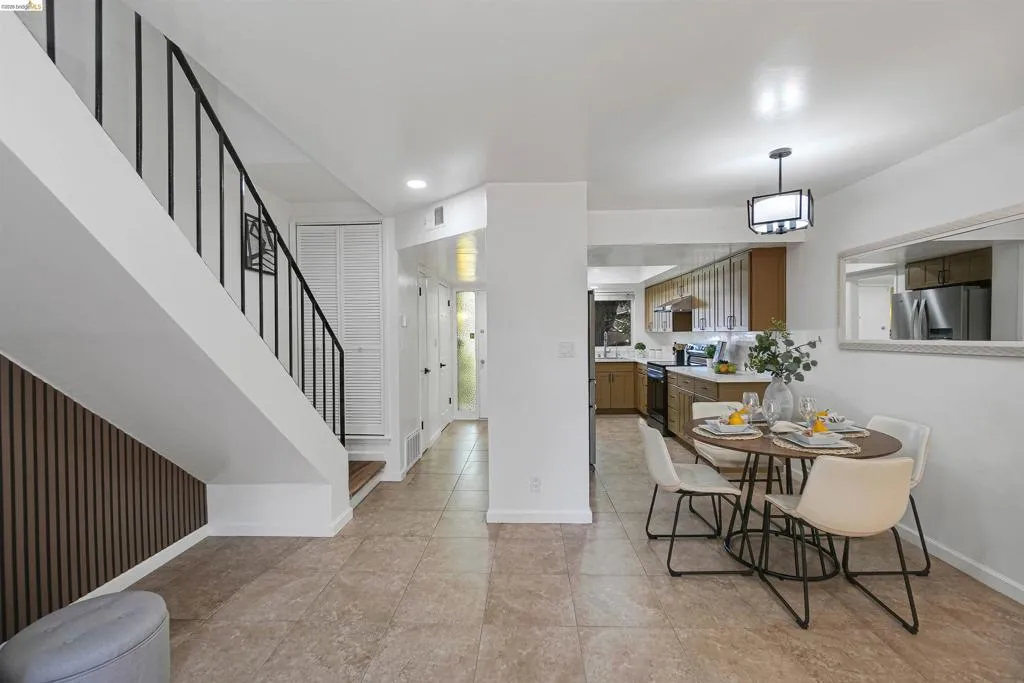 Open-concept living space with tile flooring throughout, featuring a modern staircase with black metal railings and a decorative wood-slat accent wall