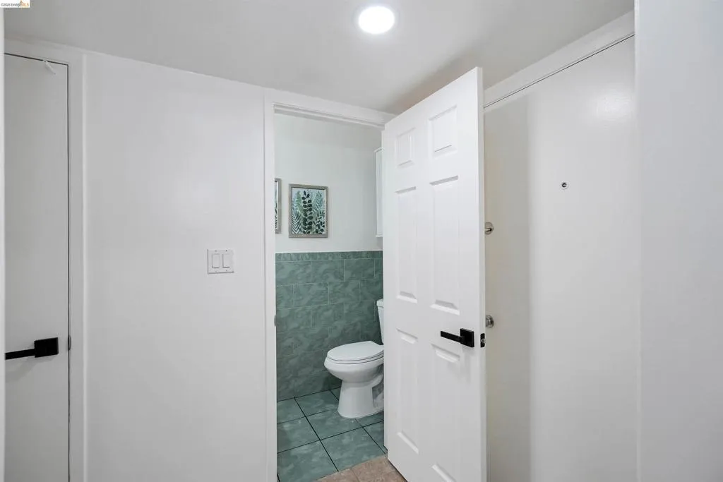 Compact bathroom featuring a white toilet, green tiled walls, and coordinating green floor tiles