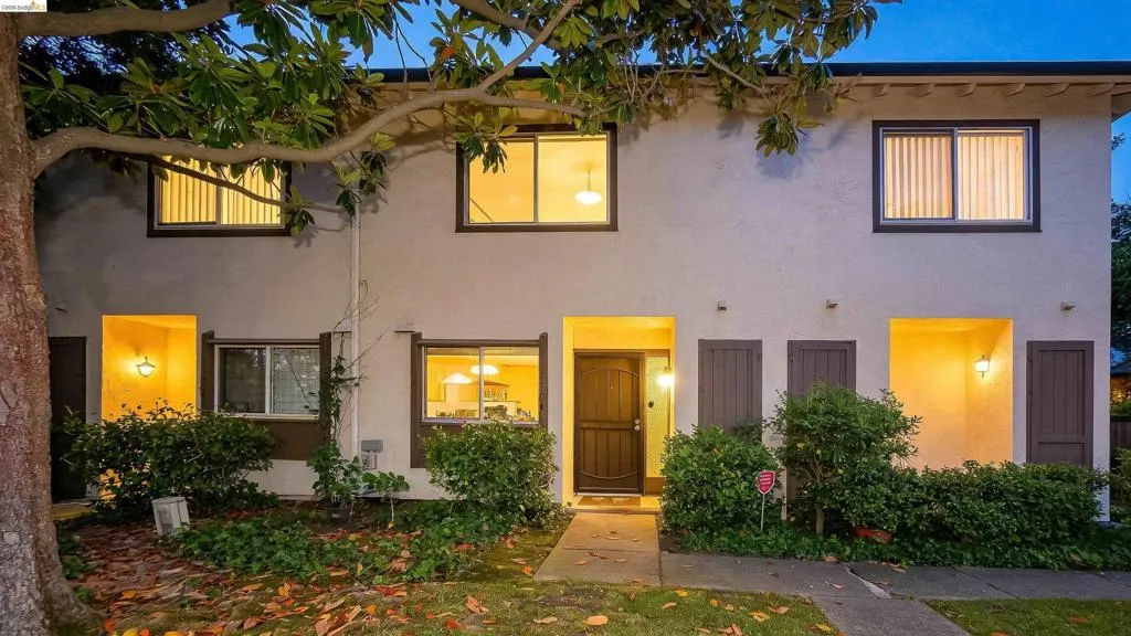 Stucco exterior featuring dual-pane windows with dark trim, a dark wood-finish entry door, and integrated exterior lighting