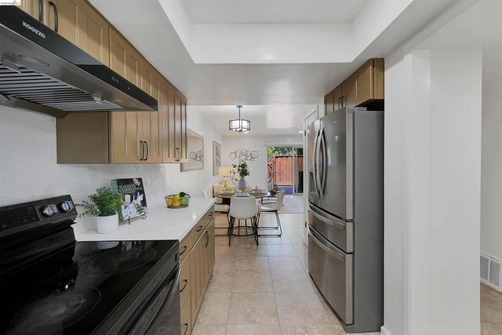 Contemporary kitchen featuring wood-finish cabinetry, white countertops, and a black electric range with a stainless steel range hood