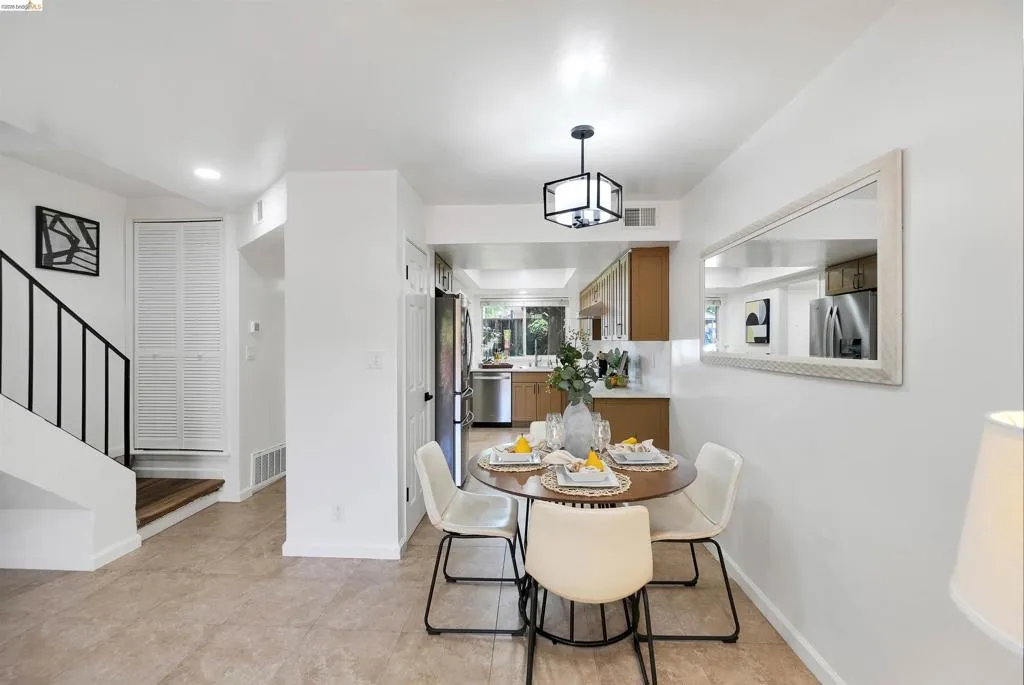 Open-concept dining area featuring tile flooring, a contemporary pendant light fixture, and a kitchen with wood cabinetry and stainless steel appliances