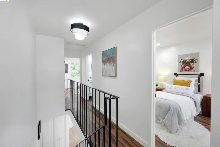 Upper-level hallway featuring wood-finish flooring, a contemporary ceiling fixture, and a black metal railing overlooking the lower level