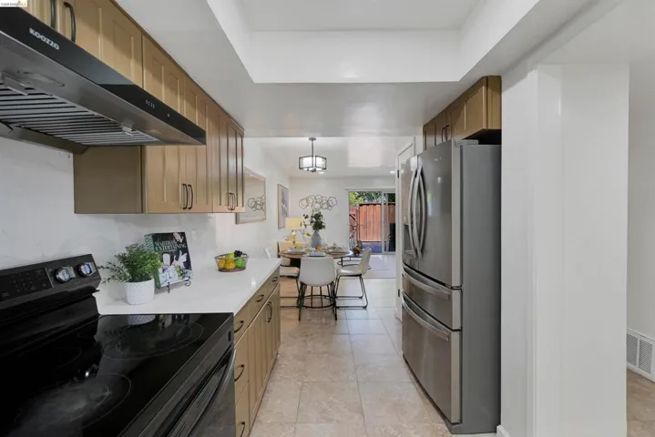 Contemporary kitchen featuring wood-finish cabinetry, white countertops, and a black electric range with a stainless steel range hood