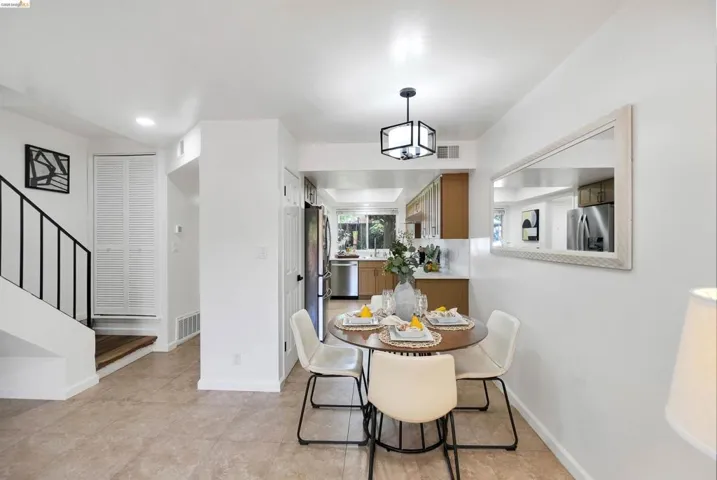 Open-concept dining area featuring tile flooring, a contemporary pendant light fixture, and a kitchen with wood cabinetry and stainless steel appliances