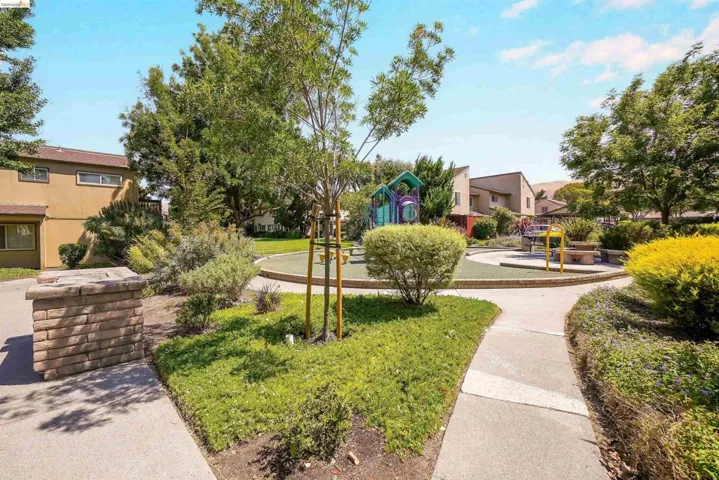 Community green space featuring a playground with colorful equipment, a circular turf area, and surrounding mature landscaping