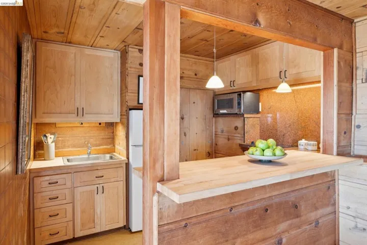 Kitchenette featuring natural wood paneling, light wood-finish cabinetry, a stainless steel sink, and an integrated wood-finish breakfast bar
