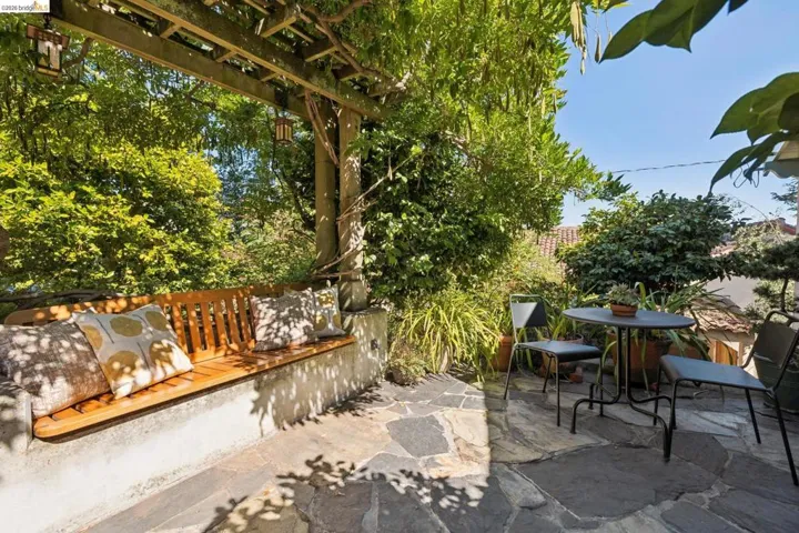 Front patio featuring a slatted wood pergola, built-in concrete bench, natural flagstone flooring, and lush landscaping.  Adjacent to dining room through French doors.