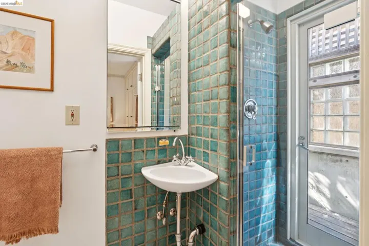 Bathroom featuring teal square wall tiles, a corner pedestal sink with chrome fixtures, and a glass-enclosed shower with a rainfall showerhead