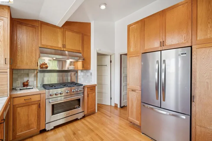 Kitchen featuring wood cabinetry, stainless steel appliances, a professional-grade gas range with a matching range hood, and a tile backsplash