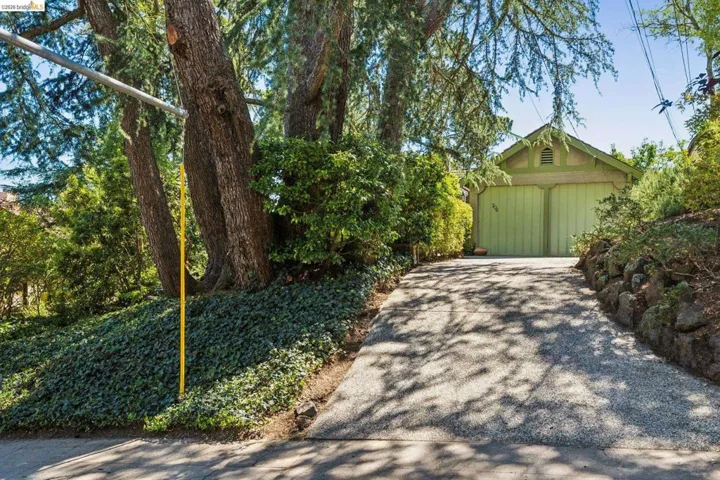 Attached garage featuring green painted doors and a gabled roof, accessed by a long gently sloping driveway