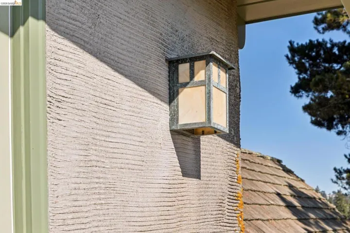 Textured exterior wall with an architectural light fixture and wood shake roofing