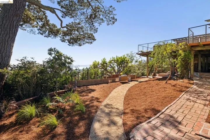 Terraced landscape featuring mulched beds, mature trees, and a brick paver pathway