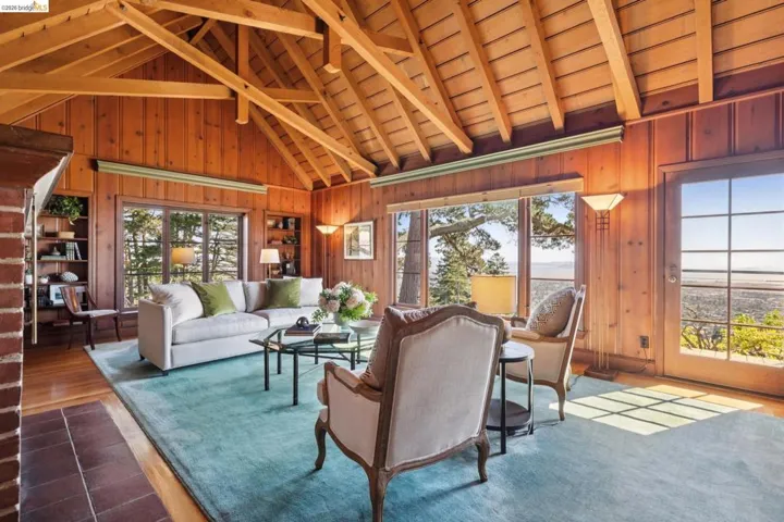 Vaulted ceiling with exposed beams, wood-paneled walls, built-in shelving, hardwood flooring, and glass-paned French doors