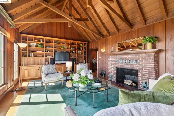 Spacious living area featuring extensive wood paneling, an exposed beam vaulted ceiling, large picture windows with Bay views, built-in shelving, fireplace and hardwood floors