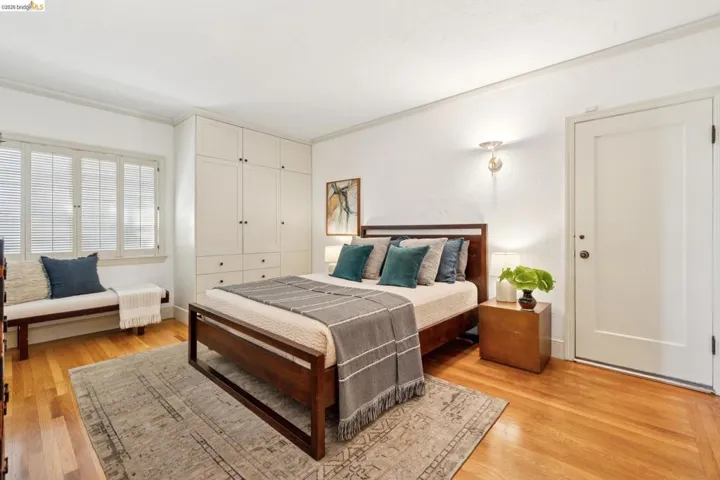 Bedroom featuring light wood flooring, built-in cabinetry with drawers and brass hardware, and three windows with louvered shutters