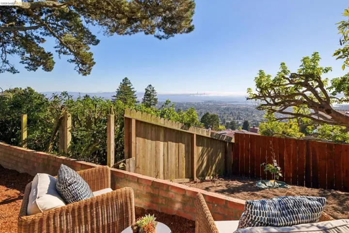 Terraced outdoor area featuring brick retaining walls, wood fencing, and established trees framing distant water and city elements