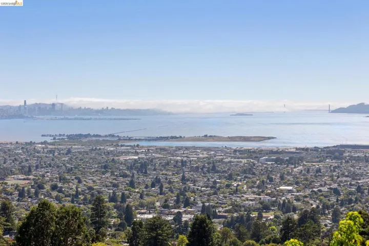 Expansive urban landscape featuring a distant city skyline, bay waters, and a bridge structure
