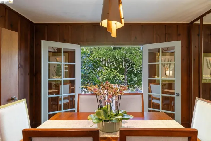 Dining area featuring wood paneled walls, a ceiling-mounted light fixture, and white French doors opening to outdoor greenery