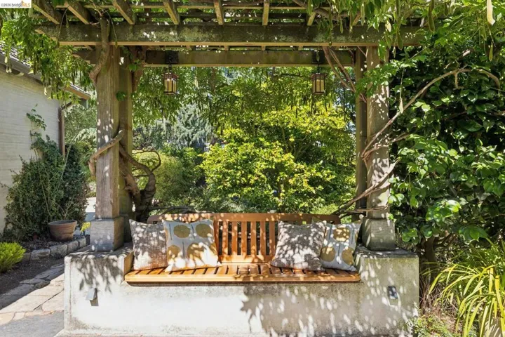 Garden pergola featuring a built-in wood bench with stone base, overhead trellis, and hanging lantern fixtures.
