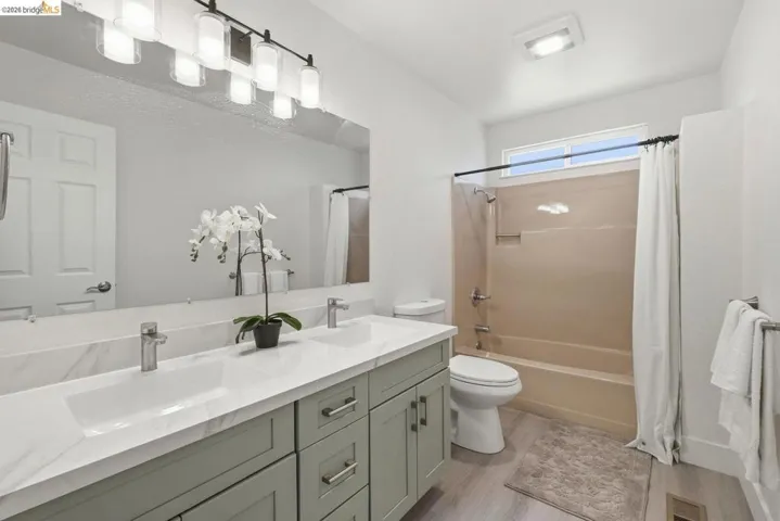 Bathroom featuring a double vanity with light green cabinetry and white countertops, a large framed mirror, a bathtub with an integrated shower, and wood-finish flooring
