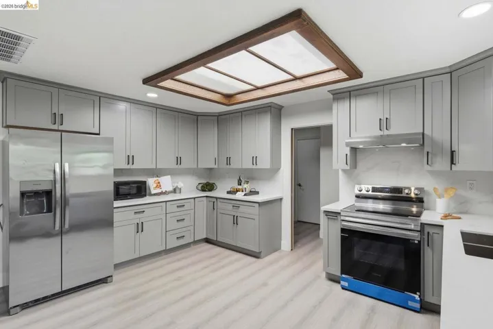 Contemporary kitchen featuring light gray shaker-style cabinetry, white countertops, and a full stainless steel appliance package