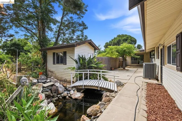 Backyard featuring a decorative pond with a white bridge, an accessory shed with horizontal siding, and a concrete pathway