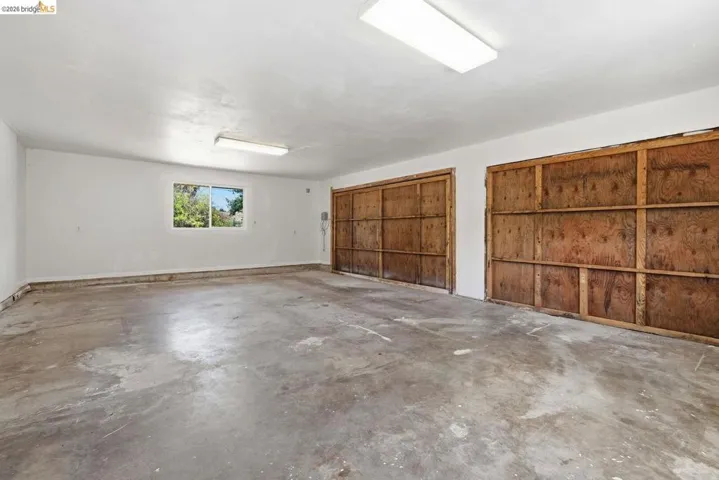 Spacious garage featuring two large wood-paneled doors, concrete flooring, overhead fluorescent lighting, and a utility sink