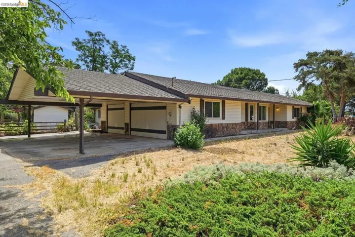 Exterior showcasing a carport with a covered driveway, a horizontal siding facade with stone accents, a covered front porch, and a brown shingle roof
