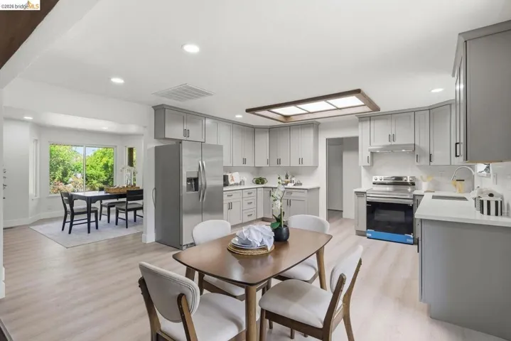 Open-concept kitchen featuring light-toned wood-finish flooring, recessed lighting, a bay window dining area, stainless steel appliances, and abundant cabinet storage